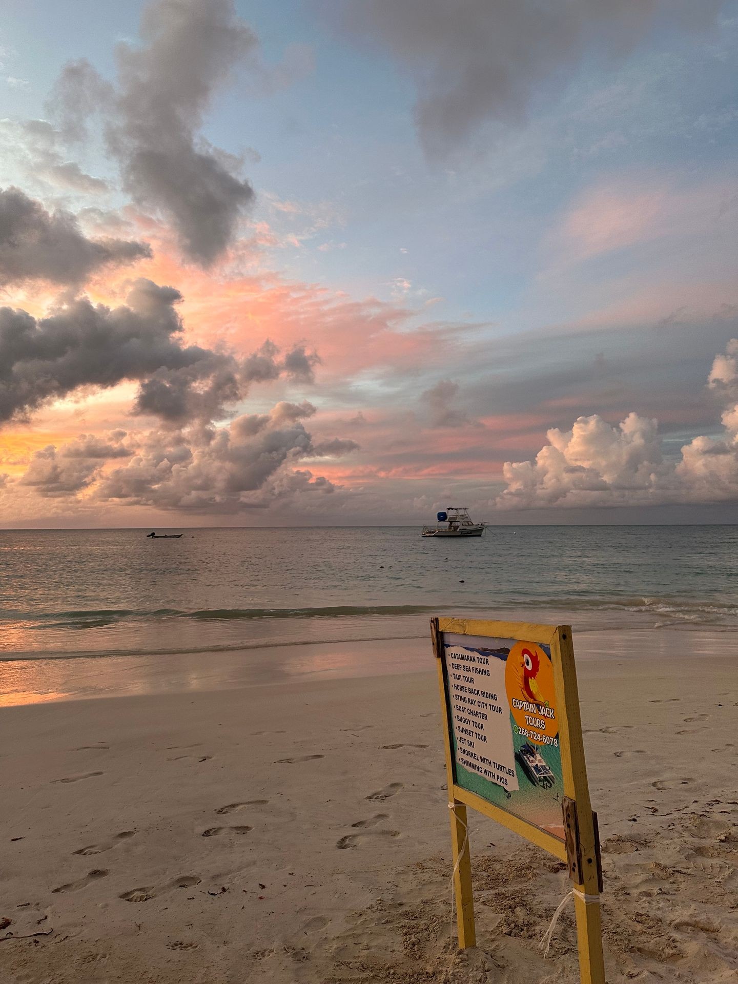 Beachfront with tour sign, boat in distance, under a colorful sunset sky with clouds.