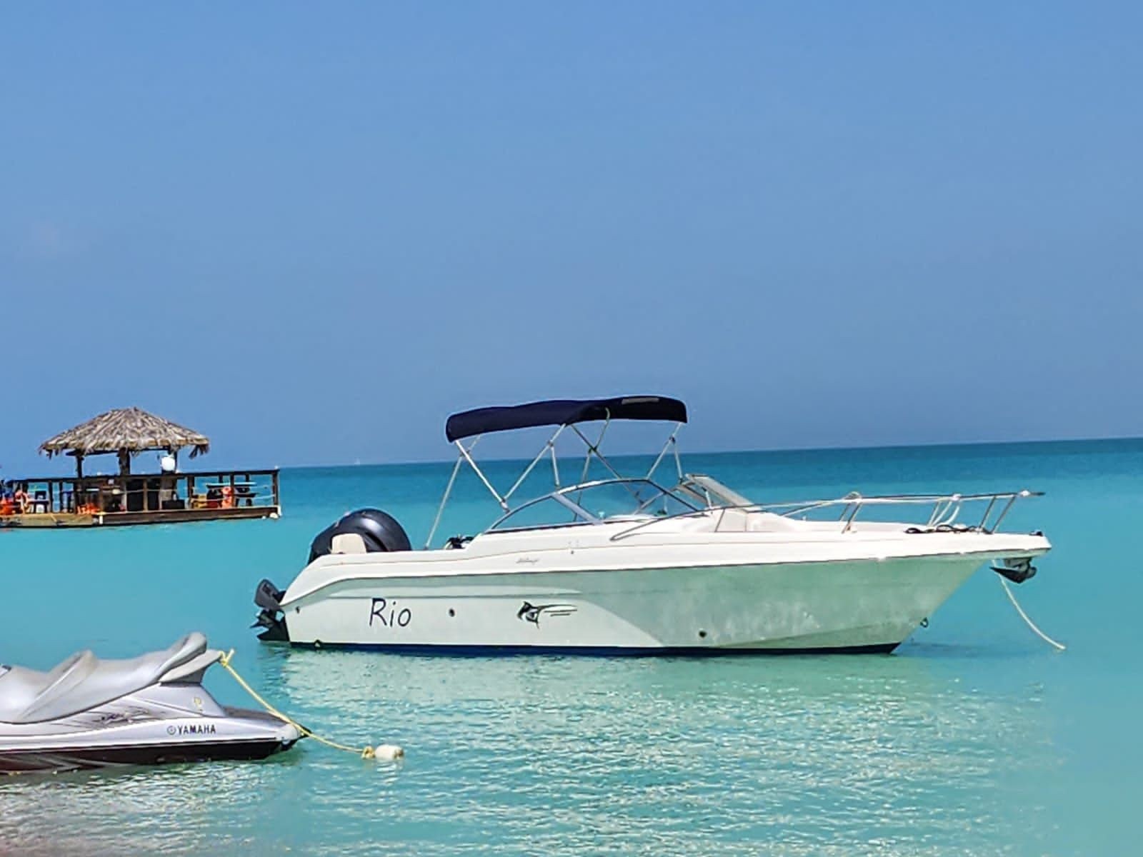 Motorboat anchored in turquoise water with a wooden hut on a floating deck in the background.