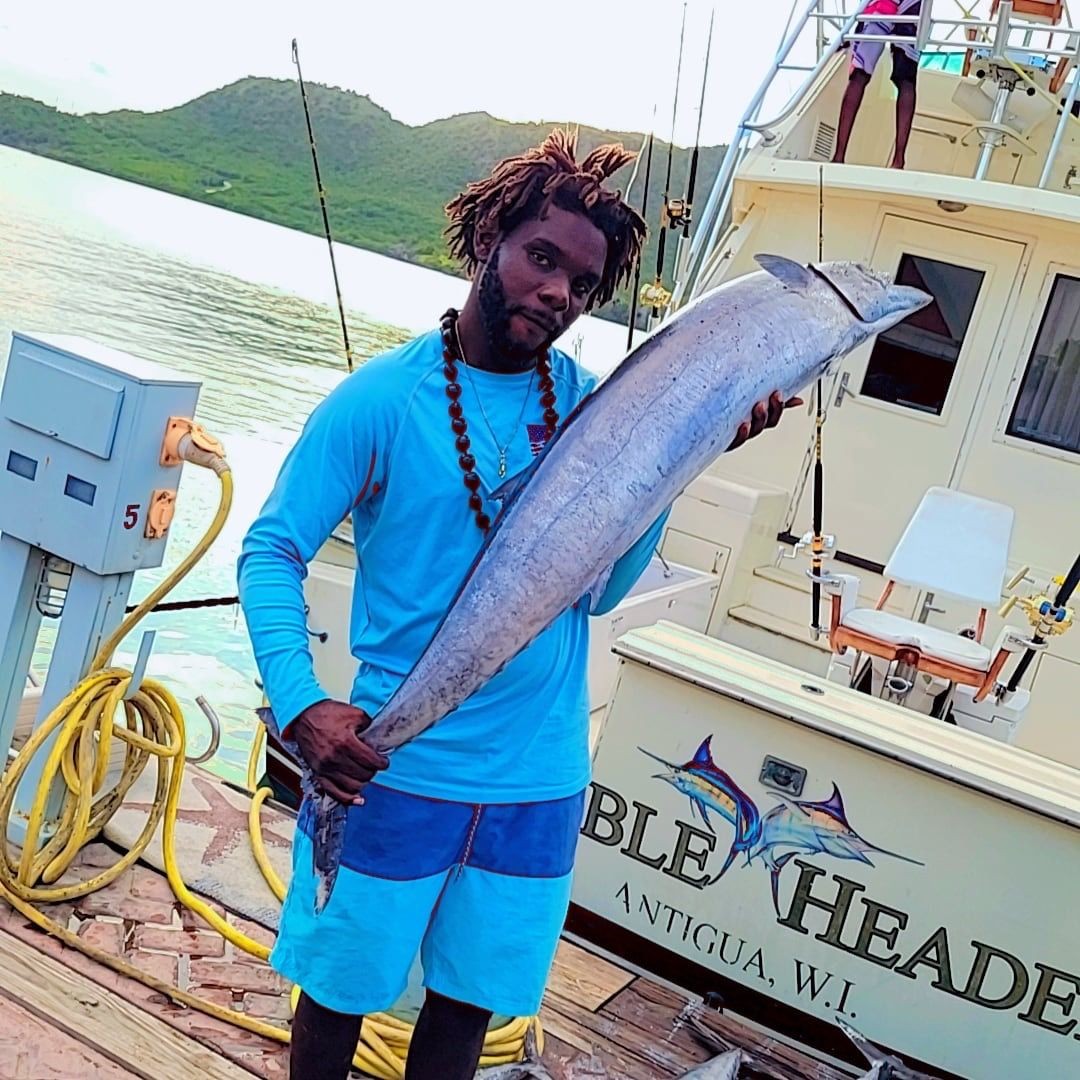 Man holding a large fish on a dock next to a fishing boat in Antigua.