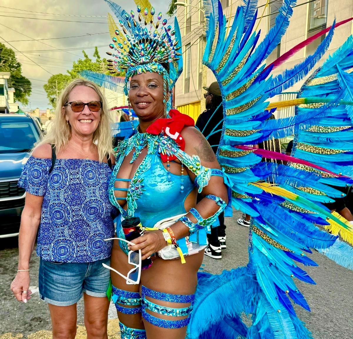 Two women smiling at a carnival; one wearing an elaborate blue feathered costume.