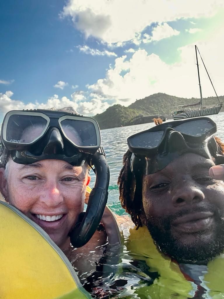 Two people wearing snorkeling gear in the ocean with a sailboat and island in the background.