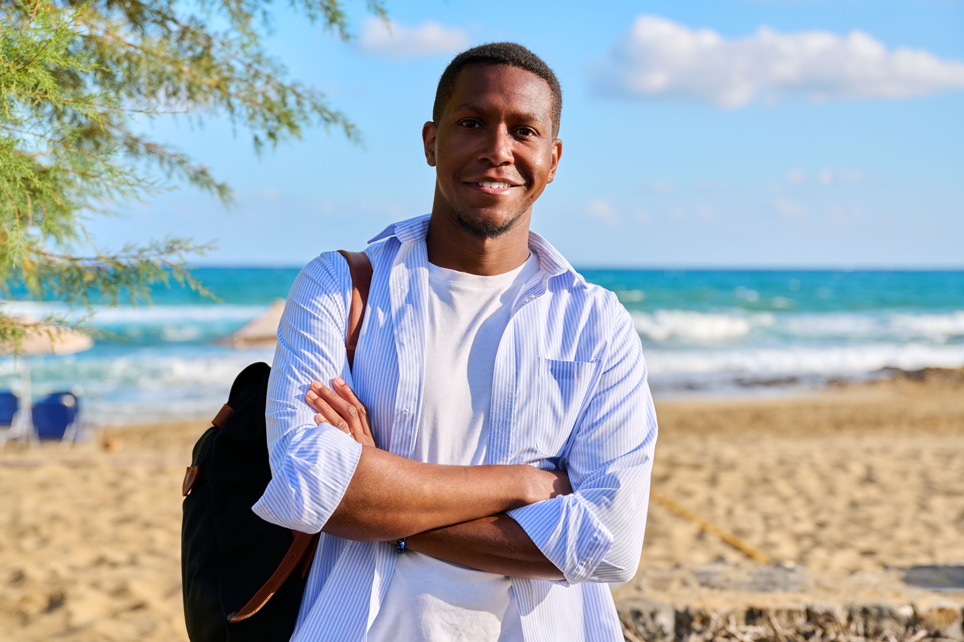 Outdoor portrait of smiling confident man with folded hands, sea nature background.